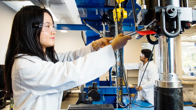 Female research student in lab coat working with mechanical engineering equipment