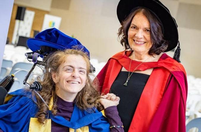 A woman in blue academic gown with a woman in red academic gown.
