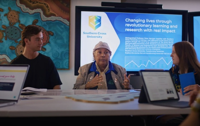 An Aboriginal elder talking to two students in a classroom setting
