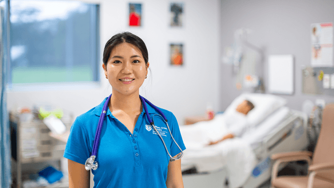 Student in blue polo with stethoscope around neck and sim doll in background