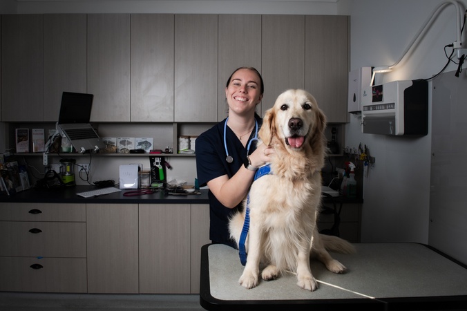 A woman in clinical scrubs with a Golden Retriever looking at the camera