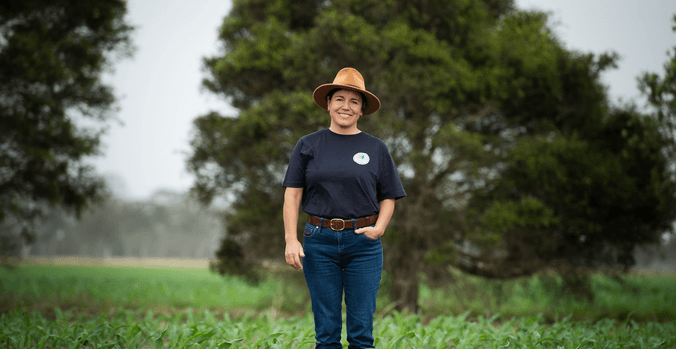Hanabeth Luke in navy shirt and hat standing in crop field