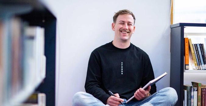Nathan smiling sitting cross-legged with notebook and pen