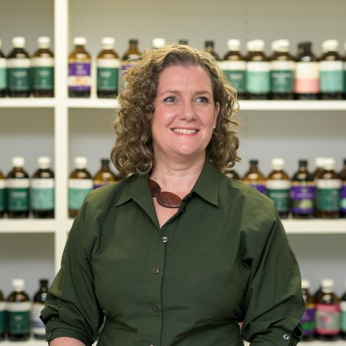 lady smiling looking away from camera, shelves of bottles behind her
