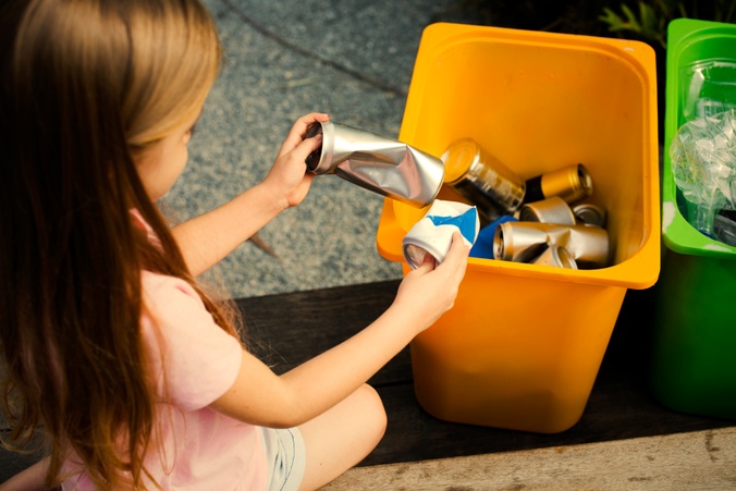 Young girl recycling cans into bin