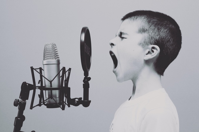 A  black and white photo of a child with short hair yelling into a recording studio microphone