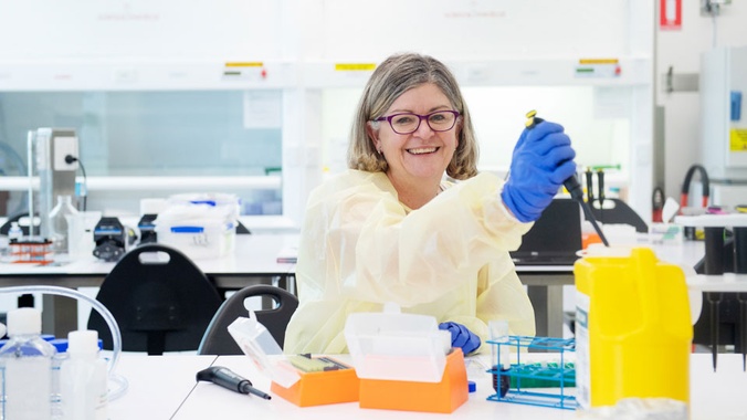 Dr Janet Schloss in research lab with syringe in hand