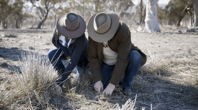 Two people wearing hats looking at soil in a paddock