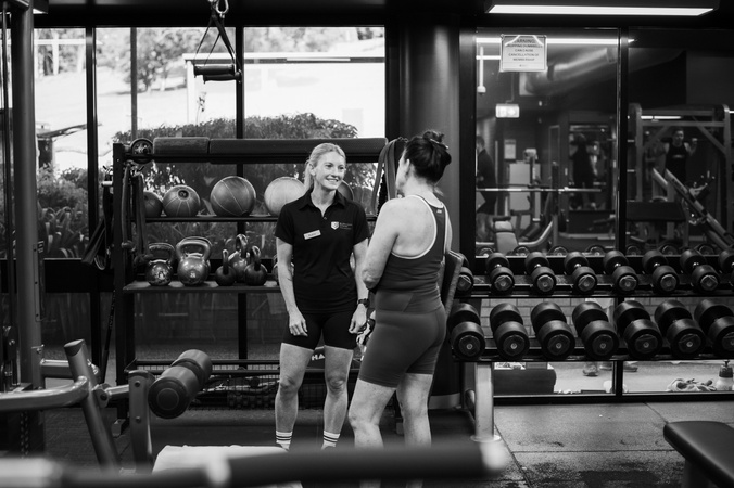 a staff member and gym member standing talking in a weight room