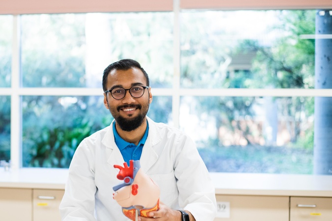 Student in lab coat holding medical prop of heart