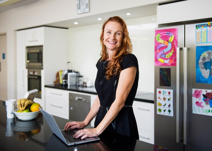 Adjunct Fellow Angela Powditch, Law alumni stands in a kitchen with an open laptop. She is smiling at the camera