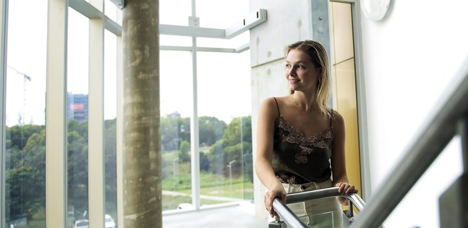 Student Lucia Miles stands on the stairs looking out the window at the Gold Coast campus