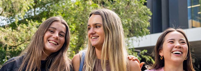 Three smiling young females with building and trees behind them