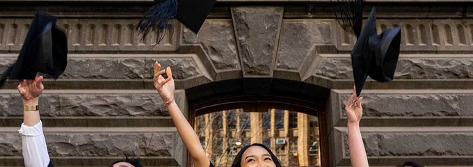 One male two female in graduation robes throwing cap in the air