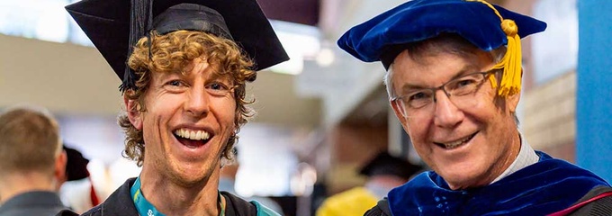 Two males in graduation robes smiling at camera