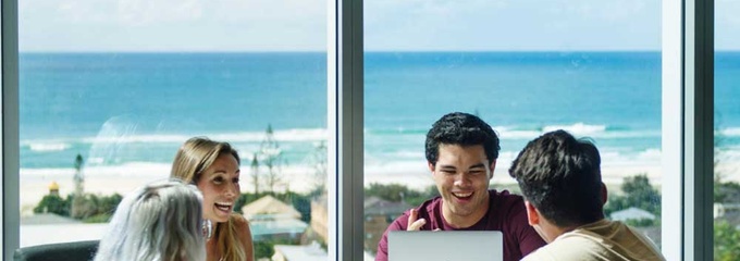 four students around a table with ocean view in the background