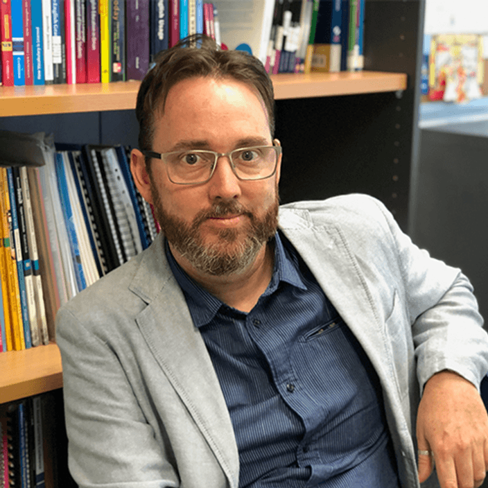 Professor Thomas Roche sitting in front of bookshelf