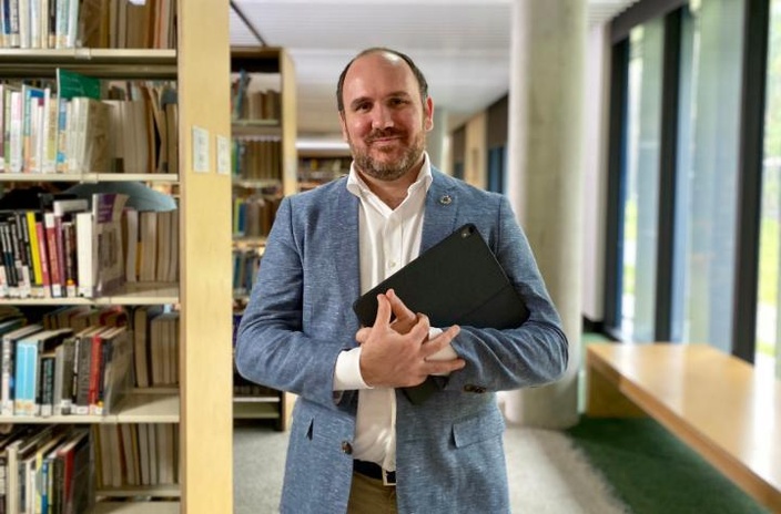 Man wearing suit holding a laptop in library