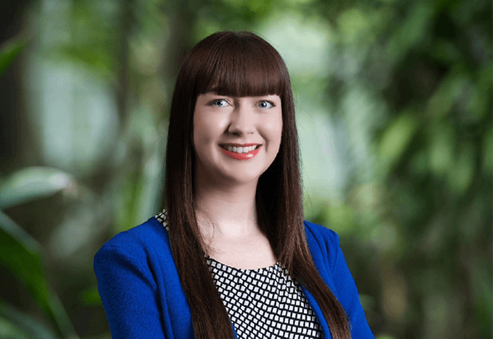 Woman smiling in blue jacket in front of greenery