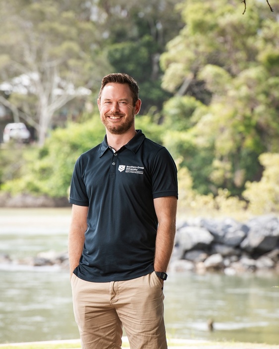 A man smiling at the camera with a stream in the background
