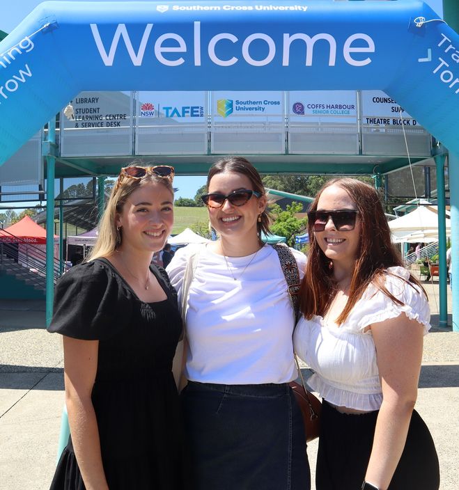 Three women smiling at the camera under a banner that says Welcome