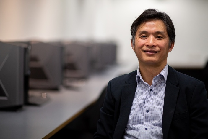 A man smiling at the camera, banks of computers in the background