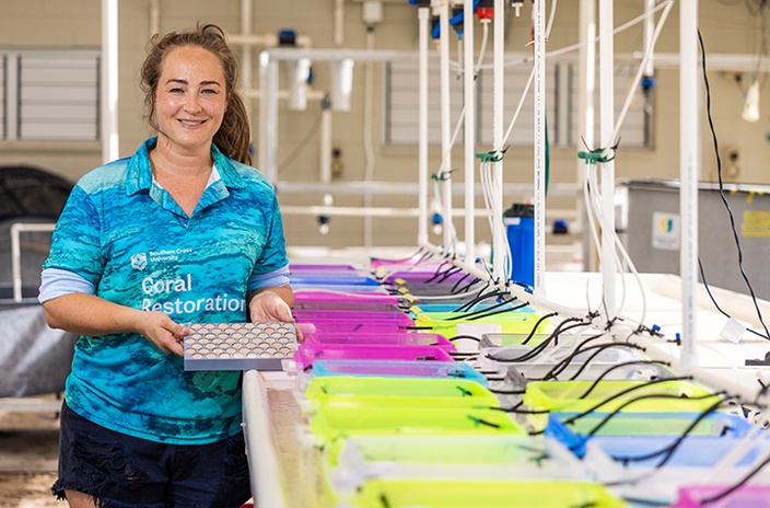 A woman in a long sleeve polo at an outside laboratory holding equipment