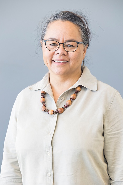 A woman with dark hair tied back, wearing glasses, a bead necklace and a beige button-up shirt