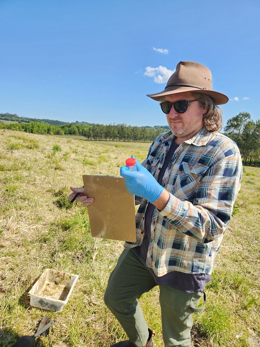 A scientist holding a specimen jar in a paddock