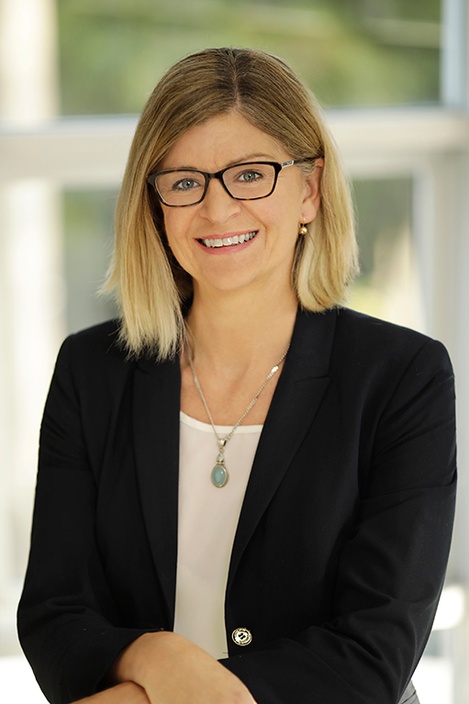 A woman with blonde hair and glasses in a black jacket and white shirt