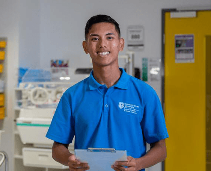 Student smiling holding clipboard in nursing lab