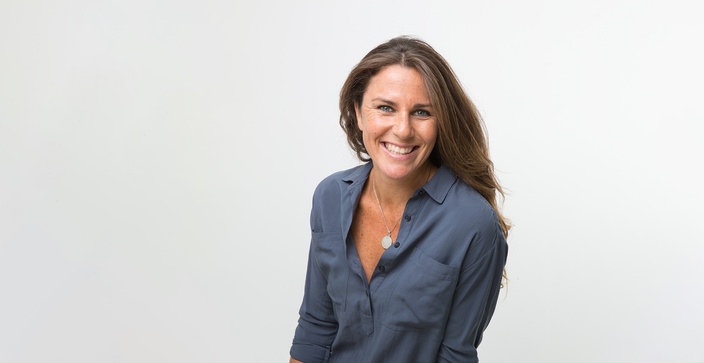 Woman standing in front of white panelling with arms crossed and smiling