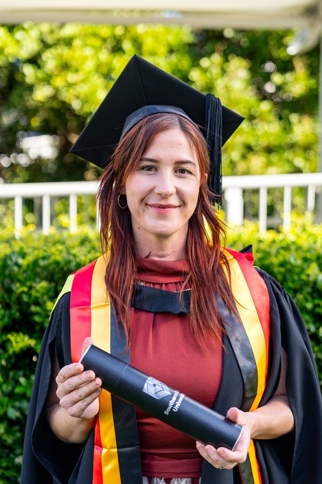 Woman in graduation robes with testamur