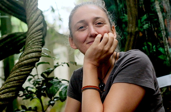 A woman sitting in a forest surrounded by tree trunks and leaves
