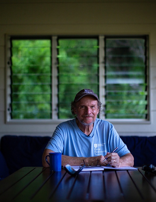 A man in a blue t-shirt and cap sitting at a desk with a pen and paper