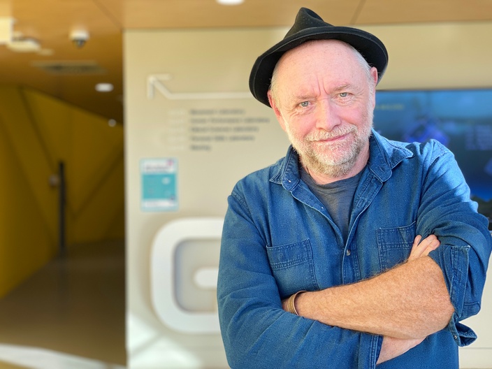 Man standing with arms crossed wearing blue shirt and black hat