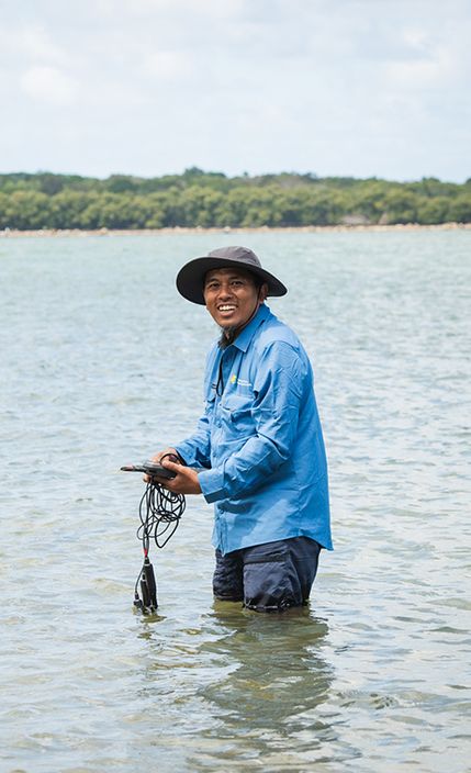A man wearing a hat and long sleeve shirt doing field work in a waterway