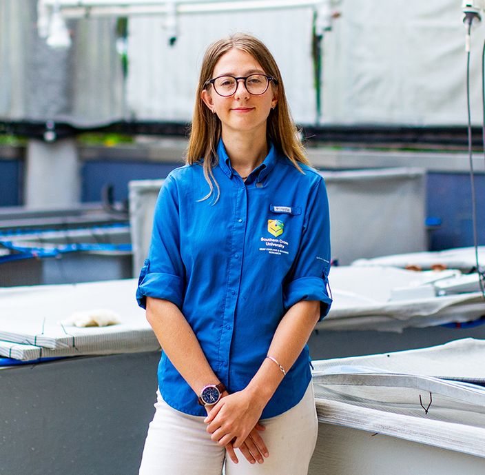 Woman in a blue shirt wearing glasses leaning against a tank