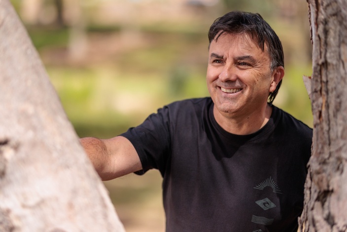 A man in a black t shirt standing against a tree trunk