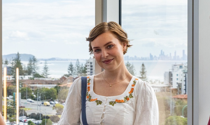 Student smiling at camera in front of window with ocean in background