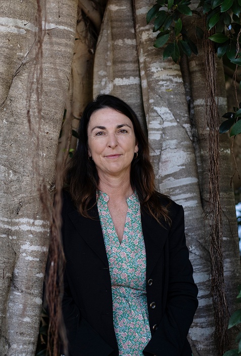 A woman wearing a black jacket in front of tree trunk