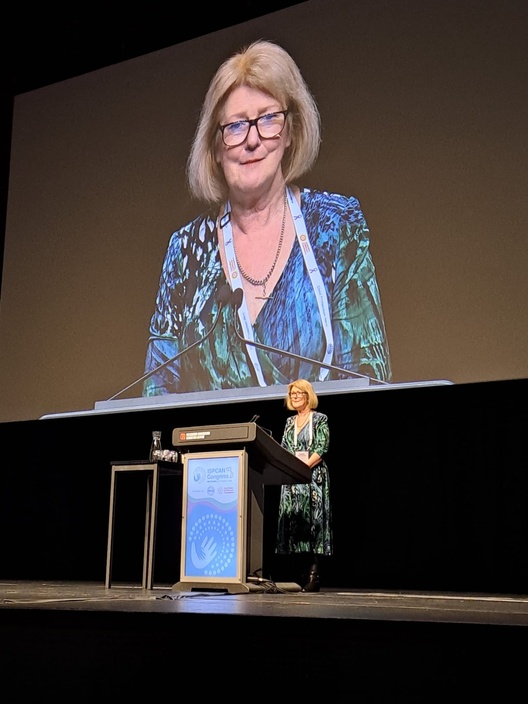 A woman making a presentation on a stage whose image is also projected on a screen behind her