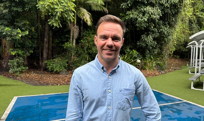 Headshot of man in blue shirt in front of greenery