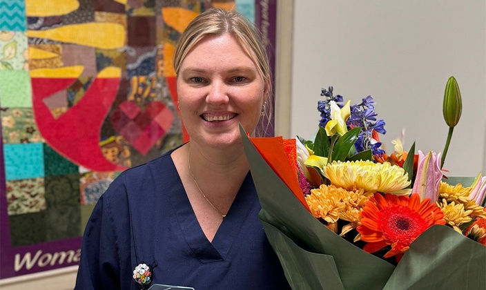 Woman in scrubs holding award and bouquet of flowers