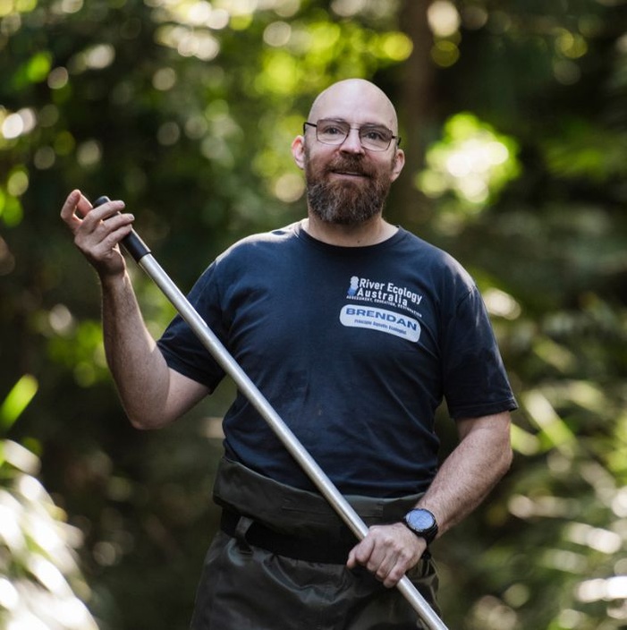 Man smiling at camera in rainforest holding a pole