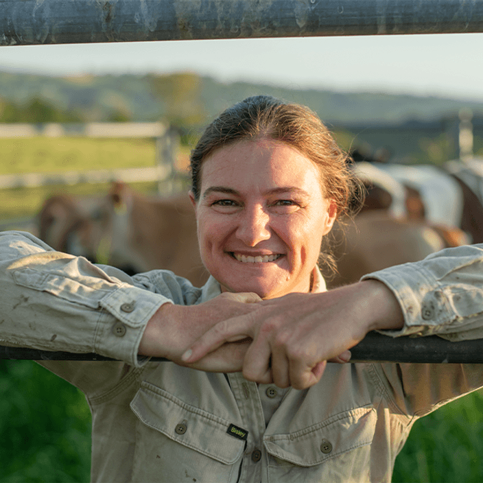 Student leaning against gate with cows in background