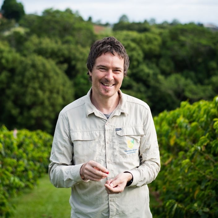 Professor Tobia Kretzschmar stands in a coffee plantation looking at camera