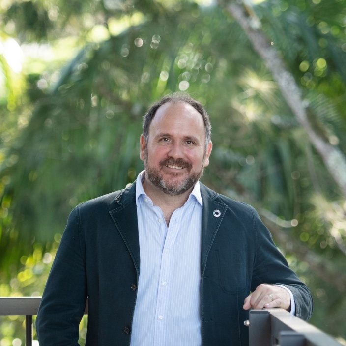 Man smiling at a camera in front of trees