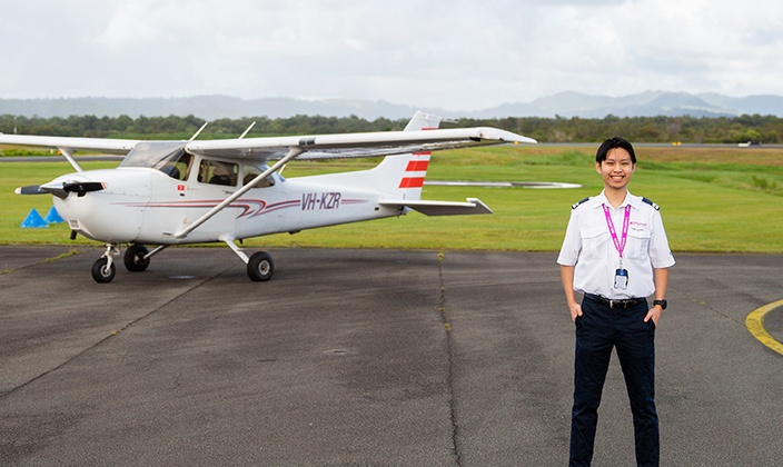 Dylan Li Tse Yu, SCU graduate smiles standing outside in front of a small white airplane on an airstrip in New South Wales