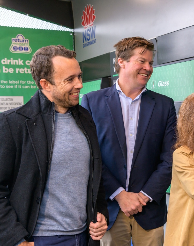 Two men watch as a woman feeds a plastics bottle into a recycling station